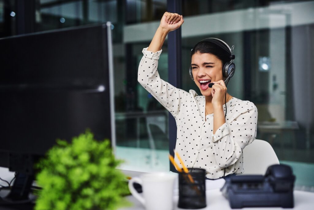Woman with headset on in office cheering with arm raise over her head